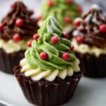 “Chocolate Christmas tree cupcake topped with green frosting, red candy ornaments, and powdered sugar snow.”