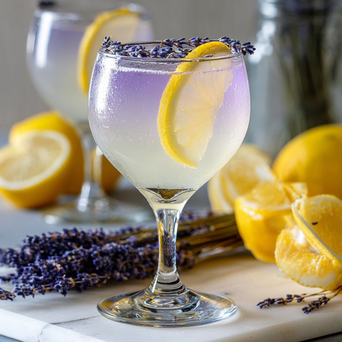 lavender limoncello spritz with a soft purple gradient, garnished with lemon slice and lavender buds on the rim, surrounded by fresh lemons and lavender flowers.