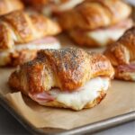 Golden baked ham and cheese croissantS on a parchment-lined tray.