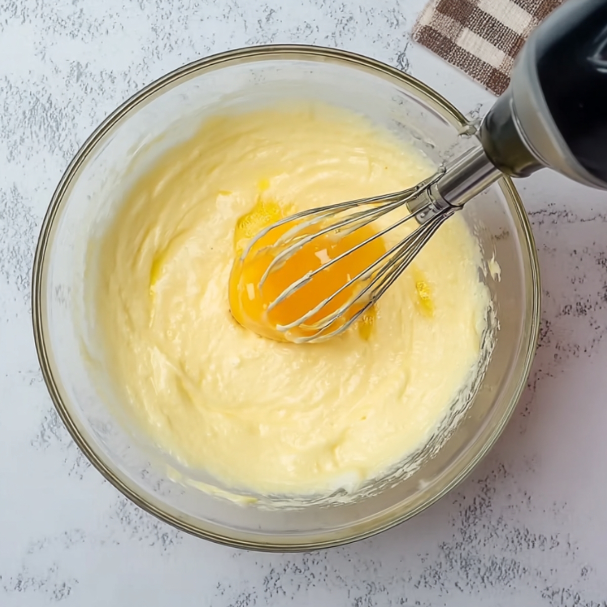 Egg yolks being whisked into creamy batter in a bowl.
