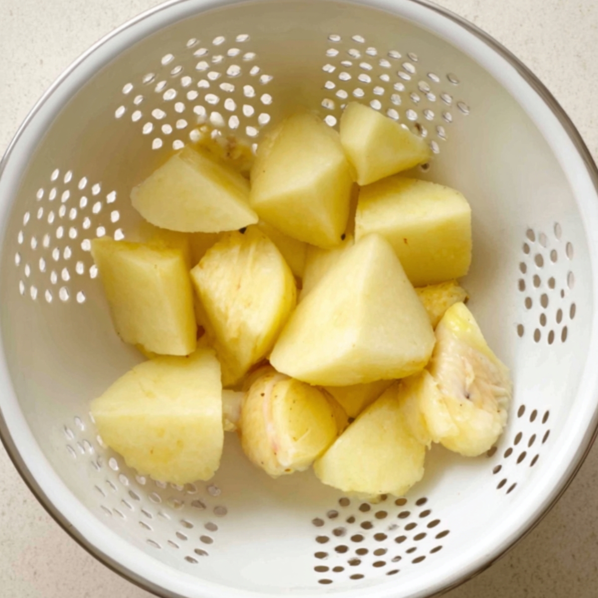 Boiled potato chunks draining in a white colander.