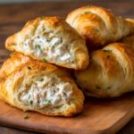 The image shows freshly baked croissants filled with a creamy Chicken Pillows ( mixture. The filling, likely made with shredded chicken and herbs, is visible inside the golden, flaky pastry. Would you like a recipe for making these chicken-filled croissants?