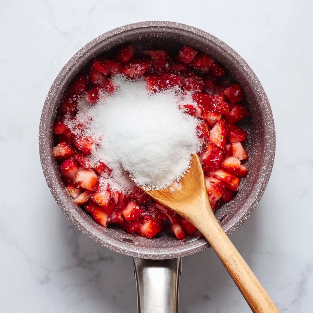 “Chopped strawberries and sugar in a saucepan with a wooden spoon.”