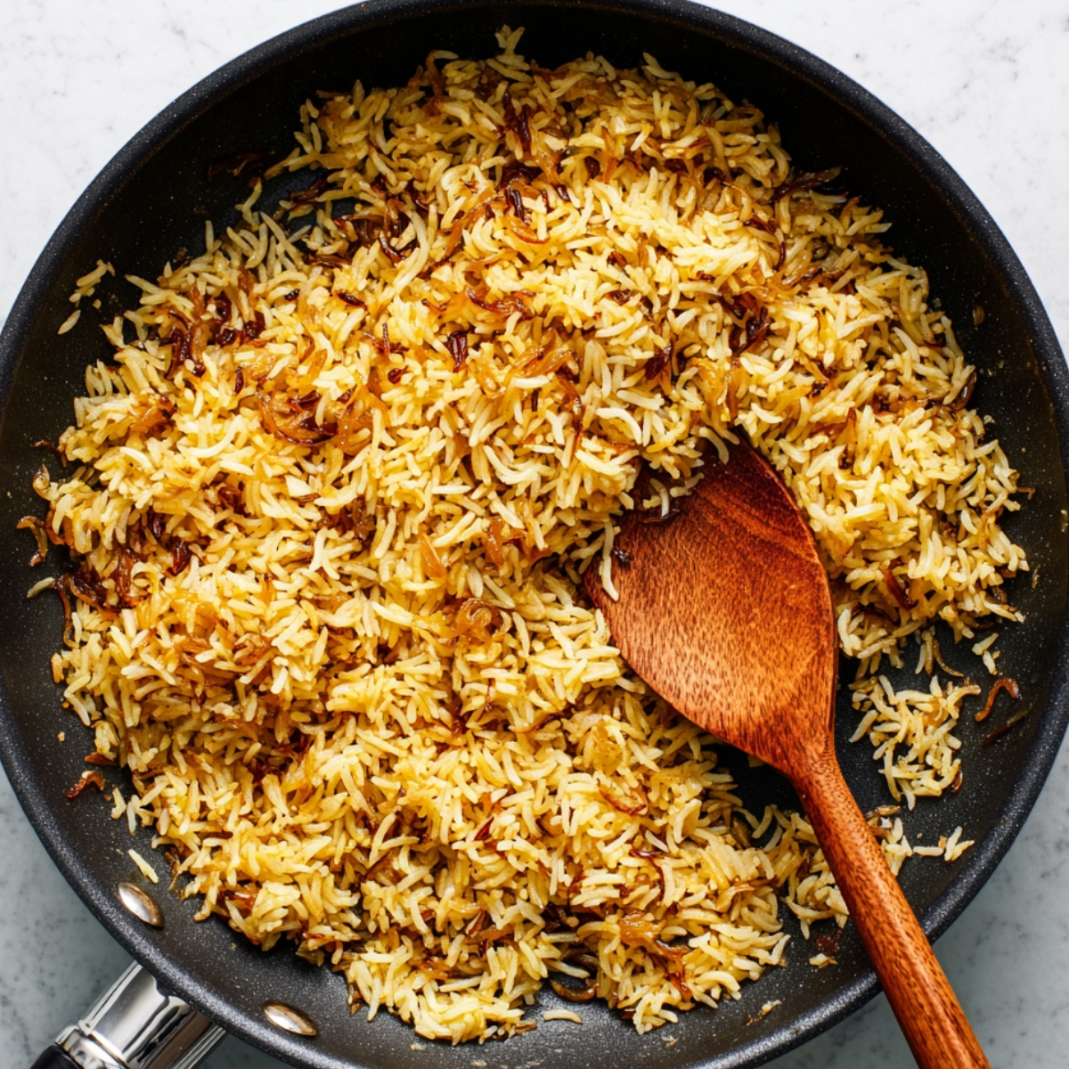 “Golden spiced rice with caramelized onions in a skillet, stirred with a wooden spoon.”