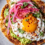 Crispy Feta Fried Eggs on a tortilla with avocado, pickled onions, cilantro, and chili flakes.