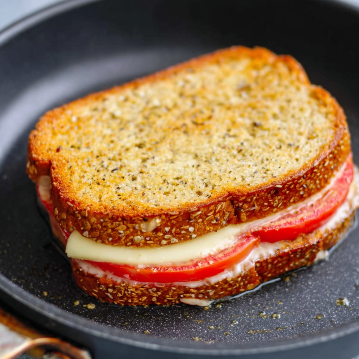 Grilled cheese sandwich with tomato slices cooking in a nonstick pan.