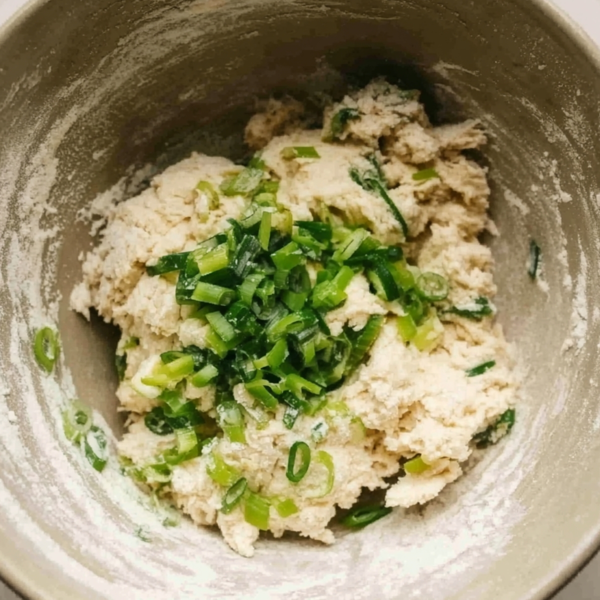 Bowl of soft potato dough mixed with chopped green onions.