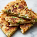 Golden-brown Irish potato farls flatbreads stacked in triangular slices on a light surface.