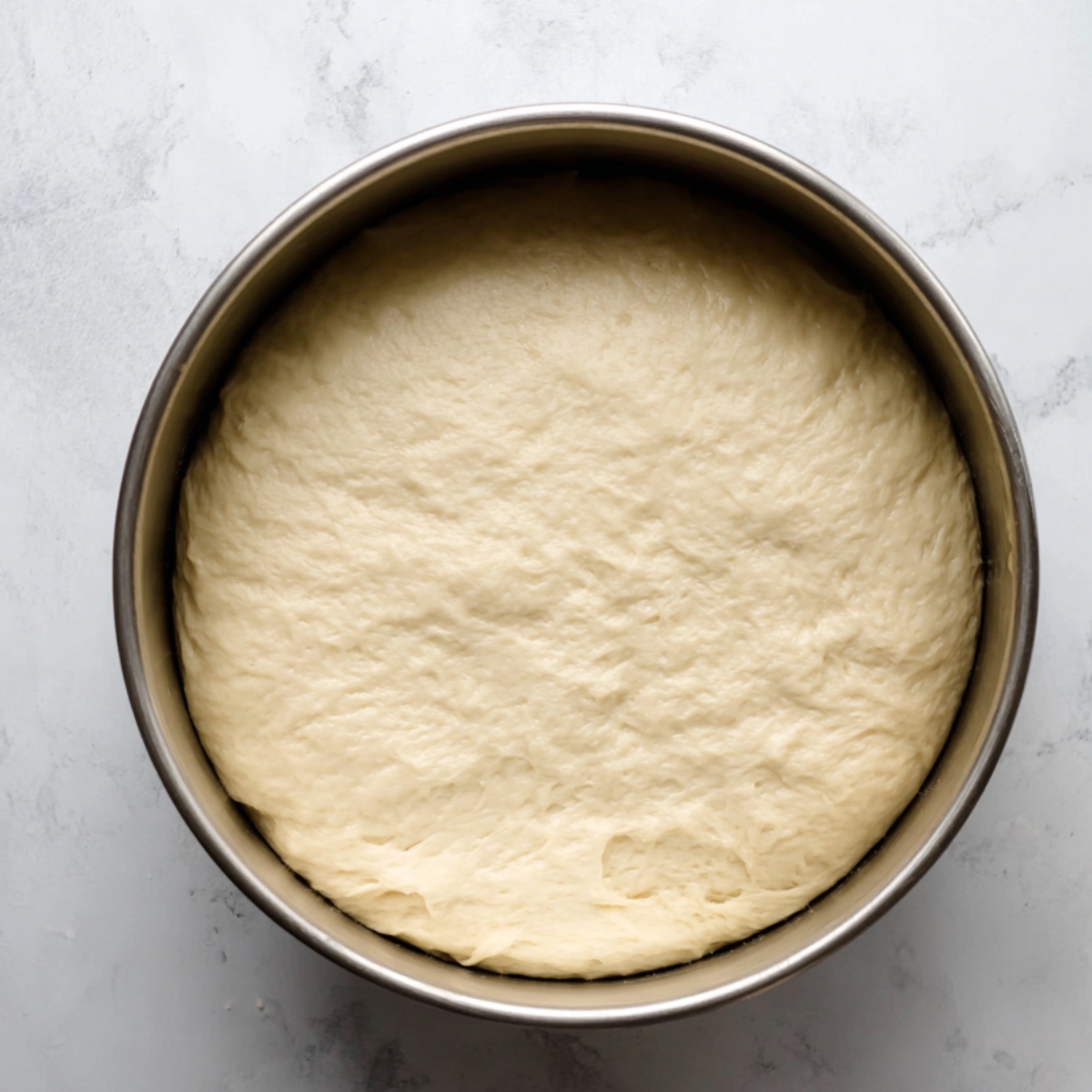 “Proofed dough risen in a metal mixing bowl.”