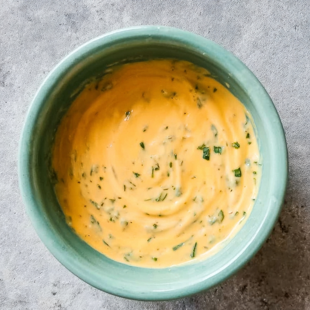 Creamy orange sauce with herbs in a small bowl.