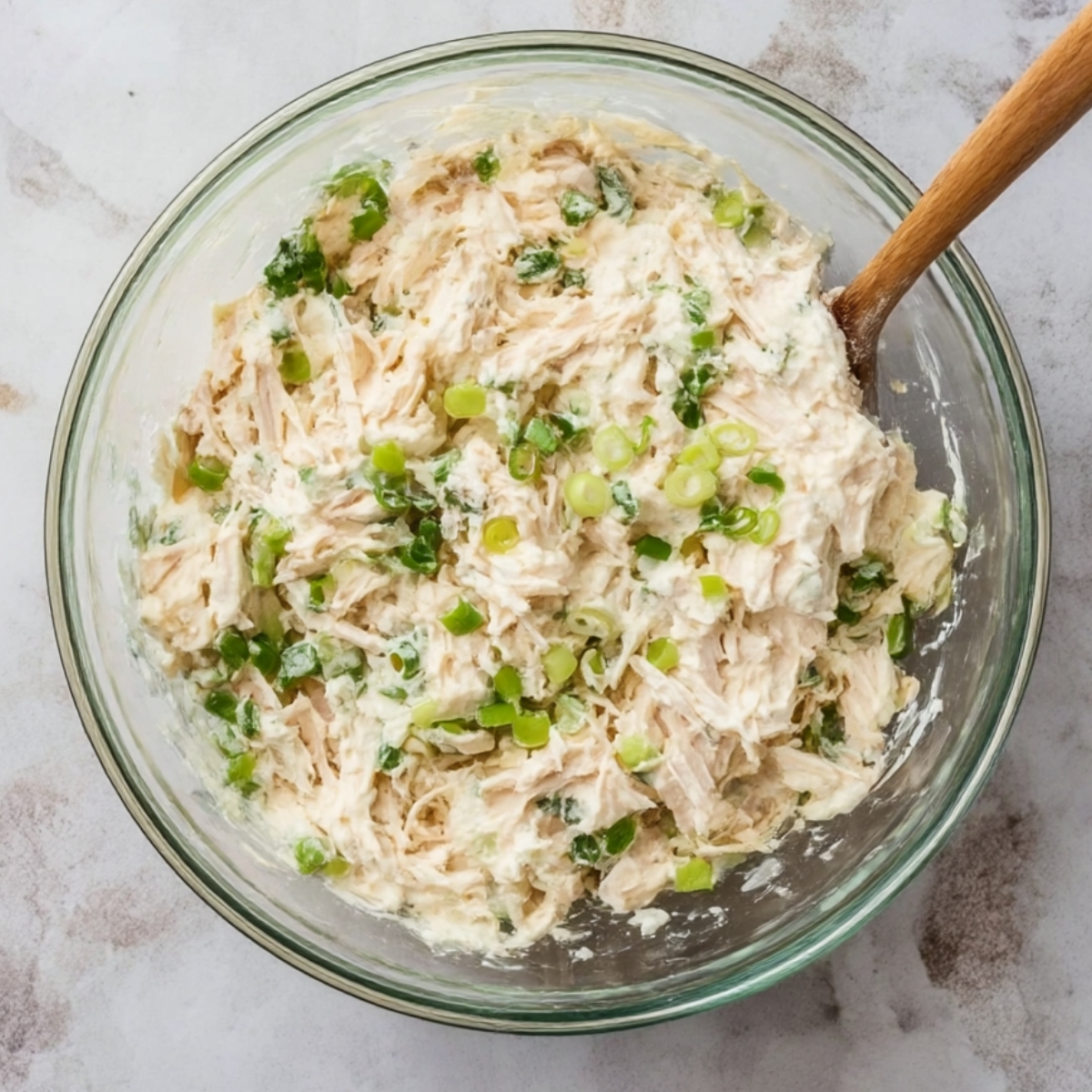 The image shows a creamy filling mixture, likely for rolls or pastries. It consists of shredded chicken, herbs, and chopped green onions, all blended together in a bowl.