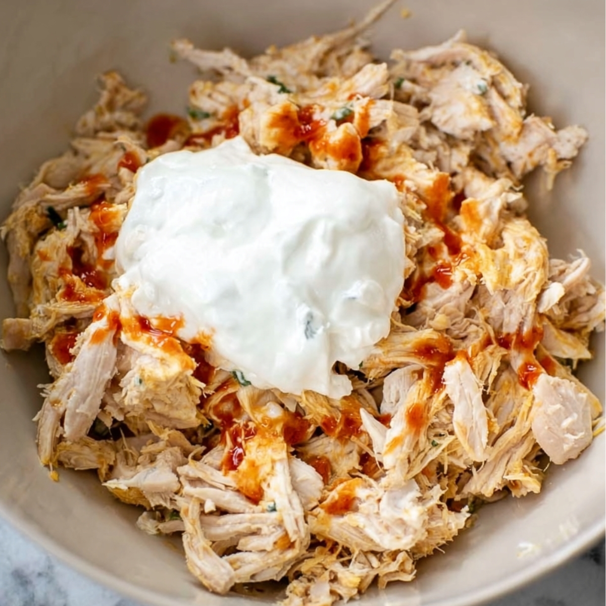 Shredded chicken mixed with sour cream and hot sauce in a bowl