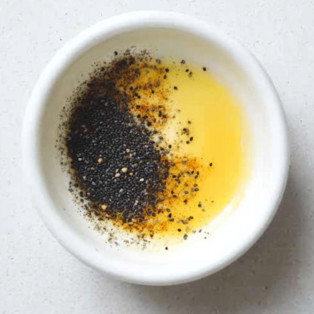 Bowl of melted butter mixed with poppy seeds and spices.