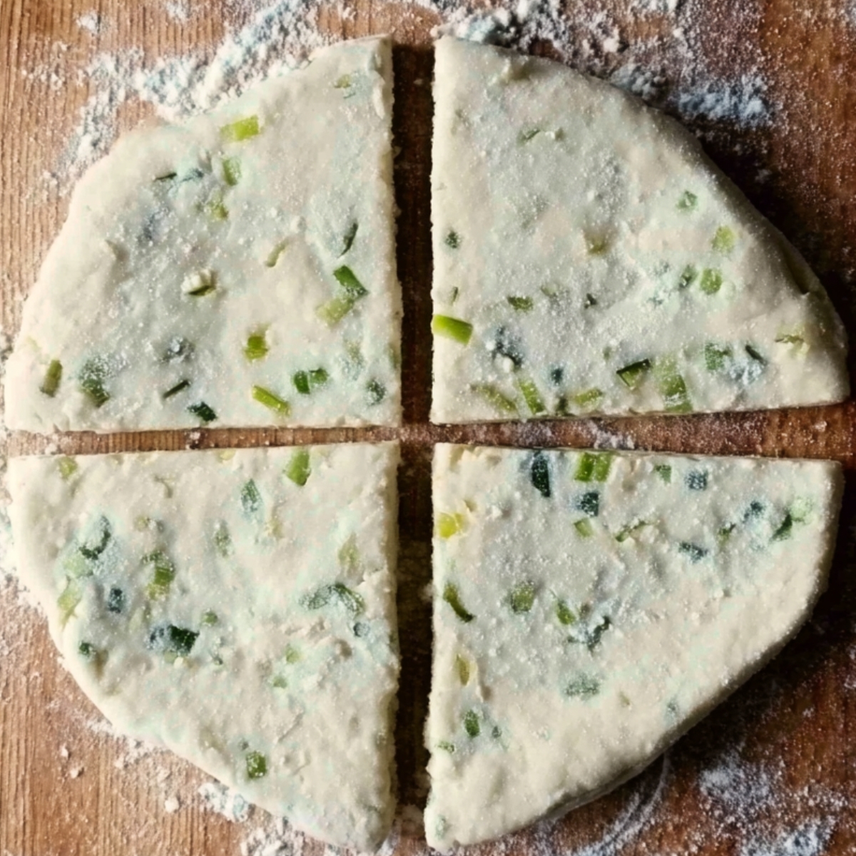 Round scallion dough cut into four equal quarters on a floured board.