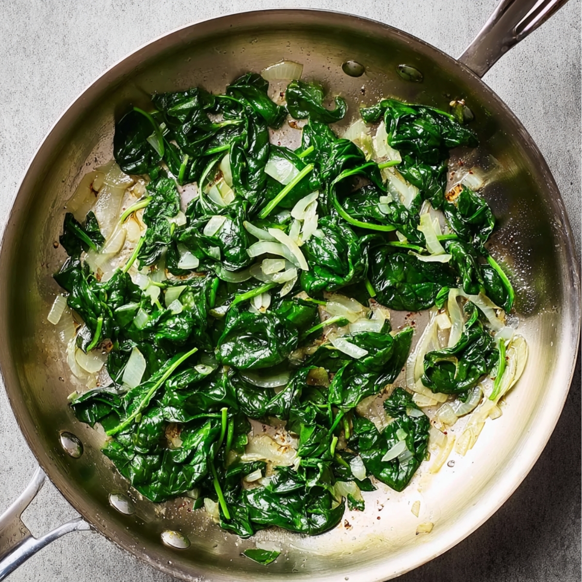 "Sauteed spinach and onions in a stainless steel pan, showing the vibrant green spinach leaves and softened onions."