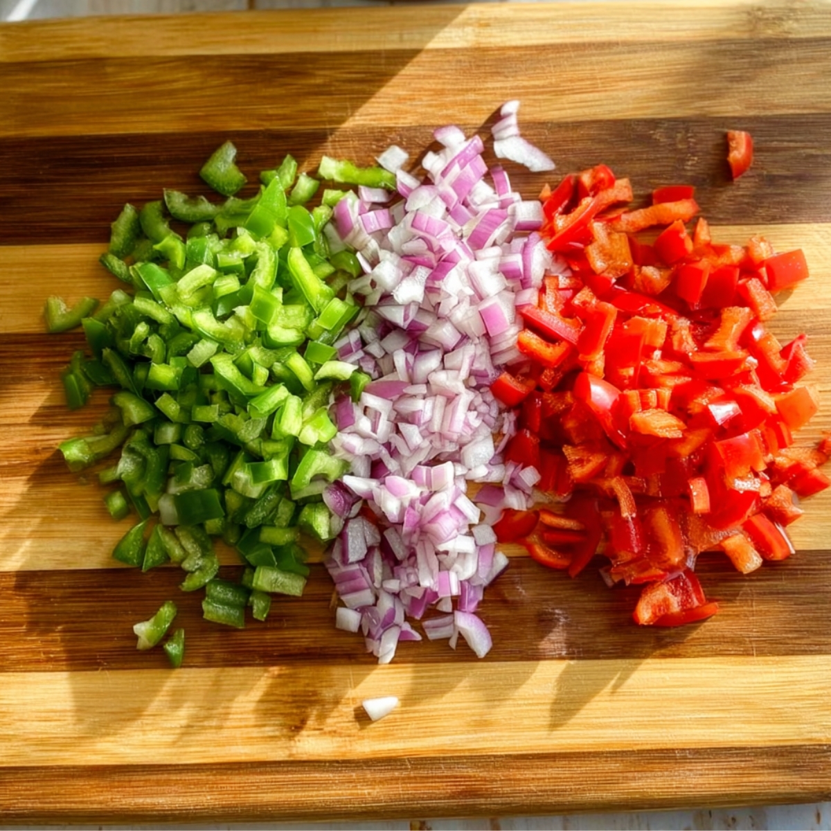 Chopped green pepper, red onion, and red bell pepper on a cutting board.