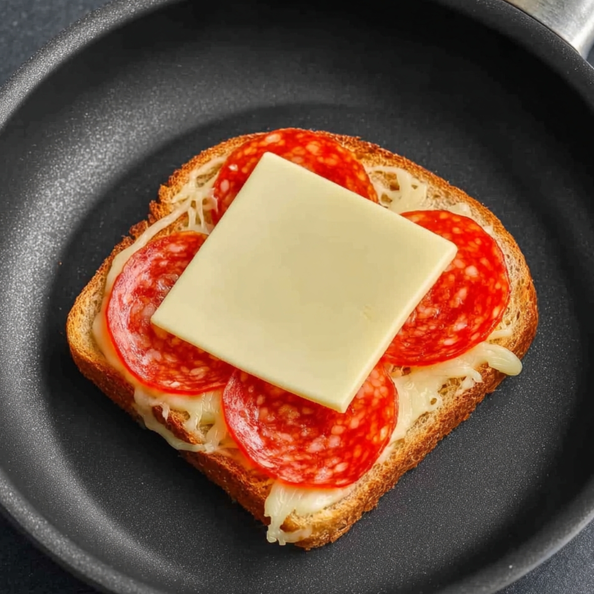 Open-faced sandwich with pepperoni and cheese cooking in a frying pan.