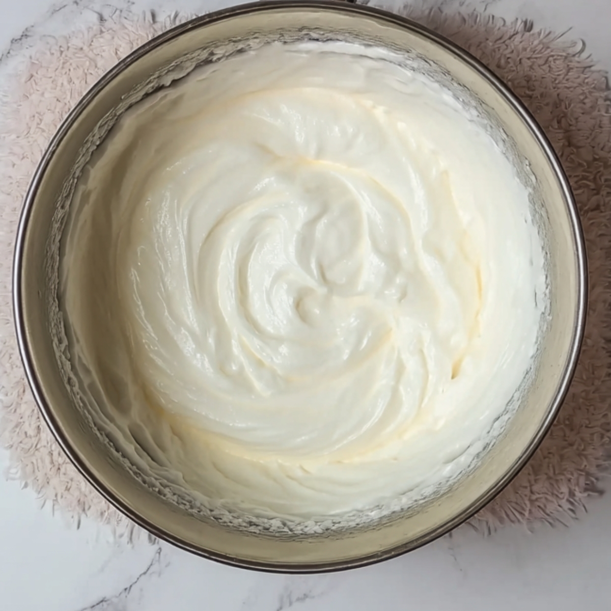 Smooth, whipped egg whites in a metal mixing bowl.