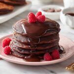 “Stack of chocolate pancakes topped with chocolate sauce and raspberries.”