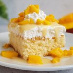 Slice of mango tres leches cake with whipped cream and mango pieces.
