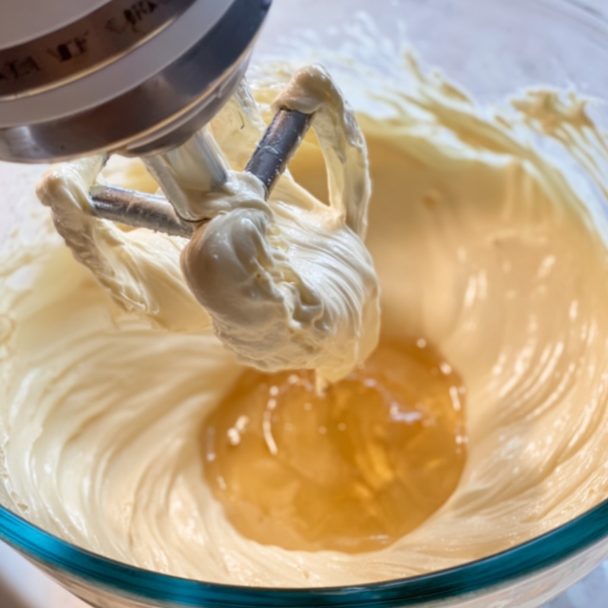 Stand mixer with paddle attachment mixing a creamy butter mixture with liquid ingredients added.