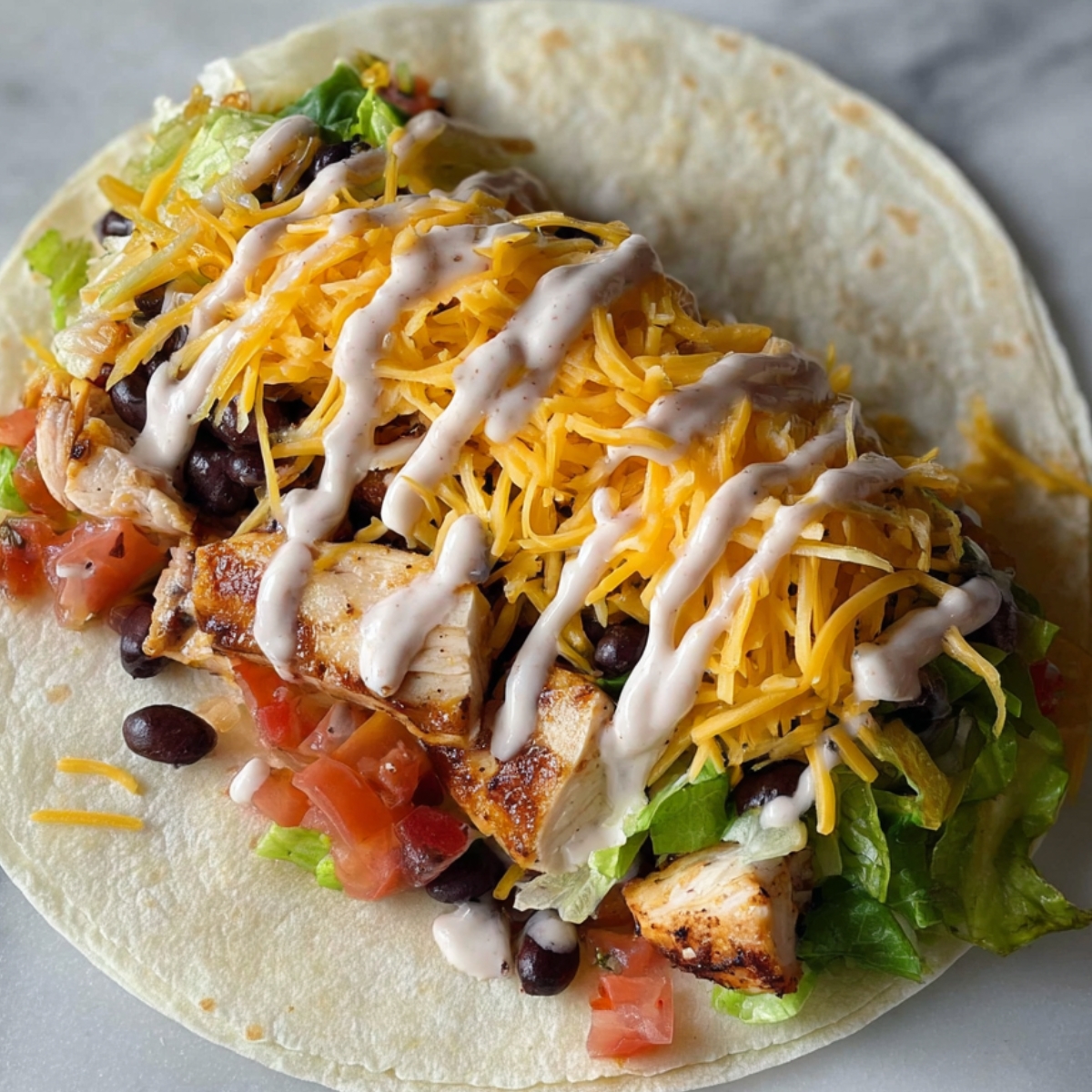 A tortilla filled with grilled chicken, black beans, shredded cheese, lettuce, tomato, and a drizzle of sauce.
