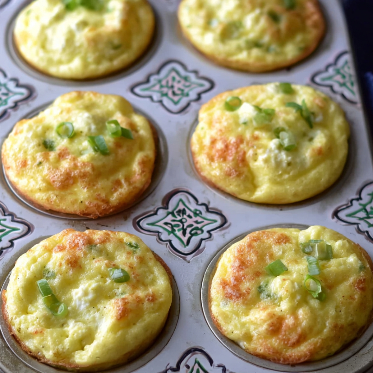 The image shows freshly baked egg muffins with green onions, resting in a muffin tin.