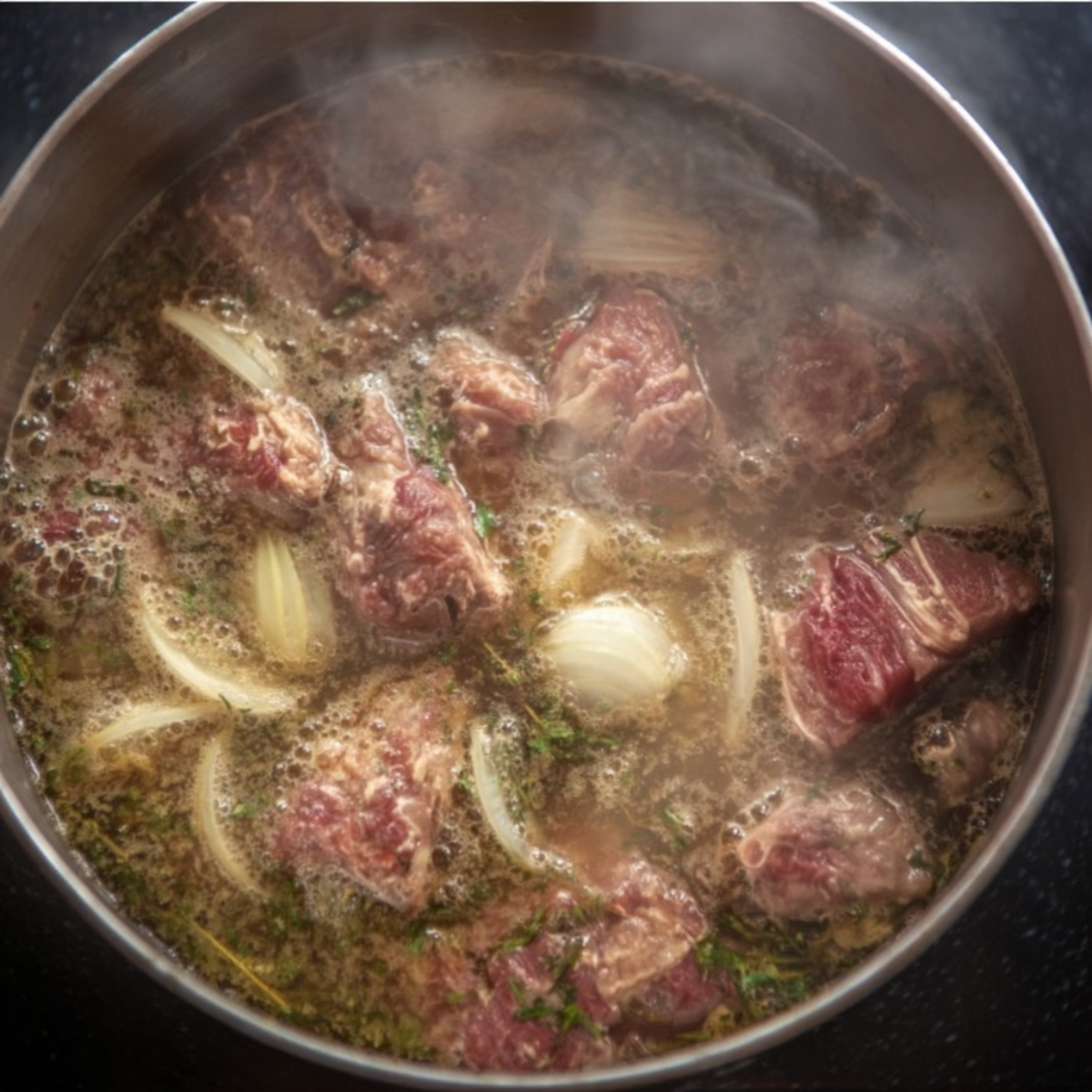 Beef chunks boiling with onions and herbs