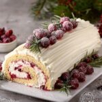 A festive Christmas raspberry cake roll Yule log cake with raspberries and powdered sugar.