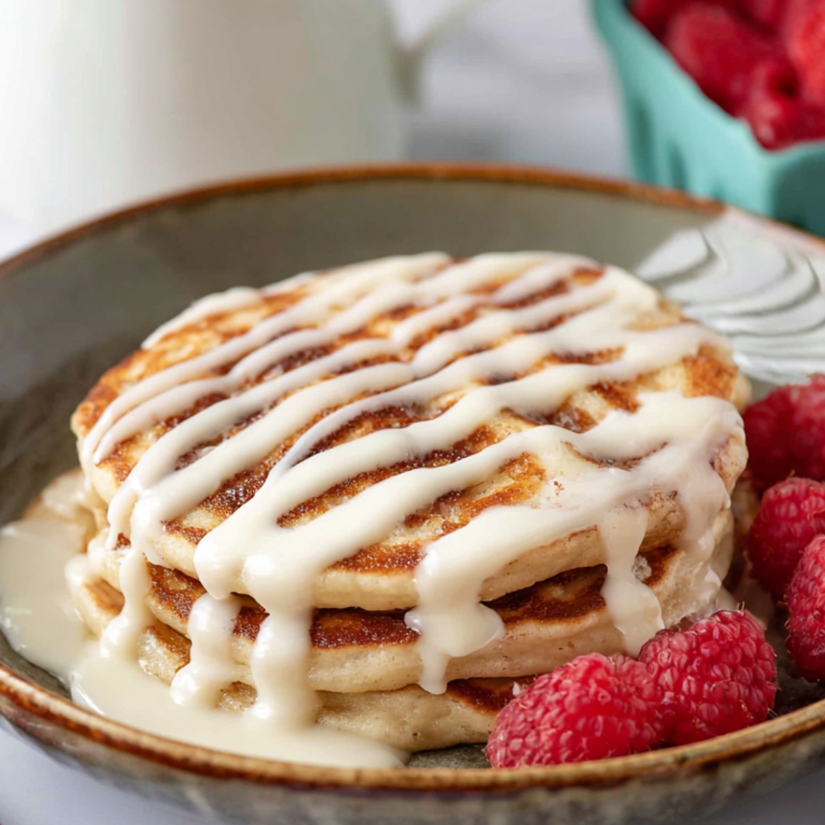 A stack of Cinnamon Roll Pancakes drizzled with icing and served with fresh raspberries.