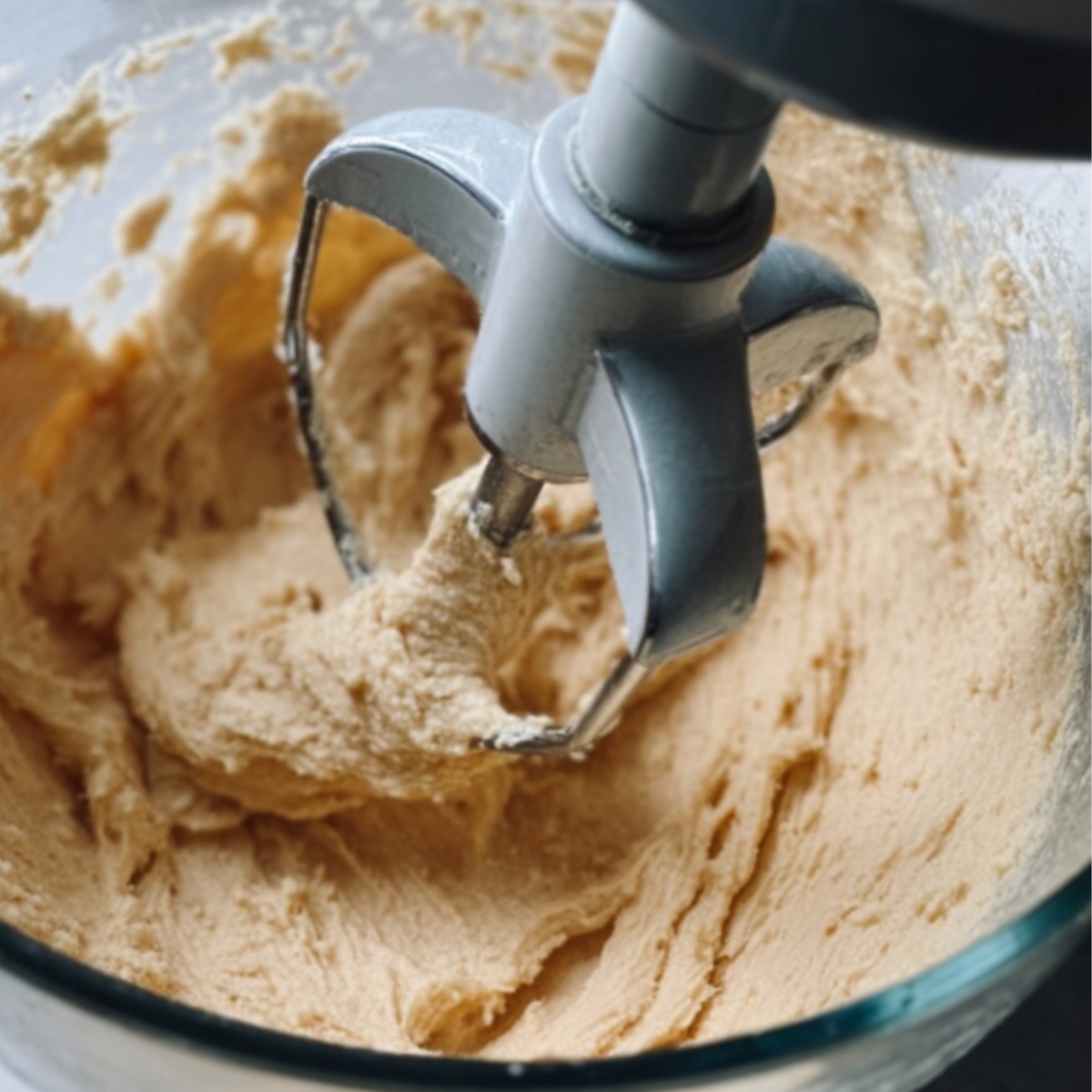 Stand mixer with paddle attachment, blending a creamy dough mixture in a glass bowl.