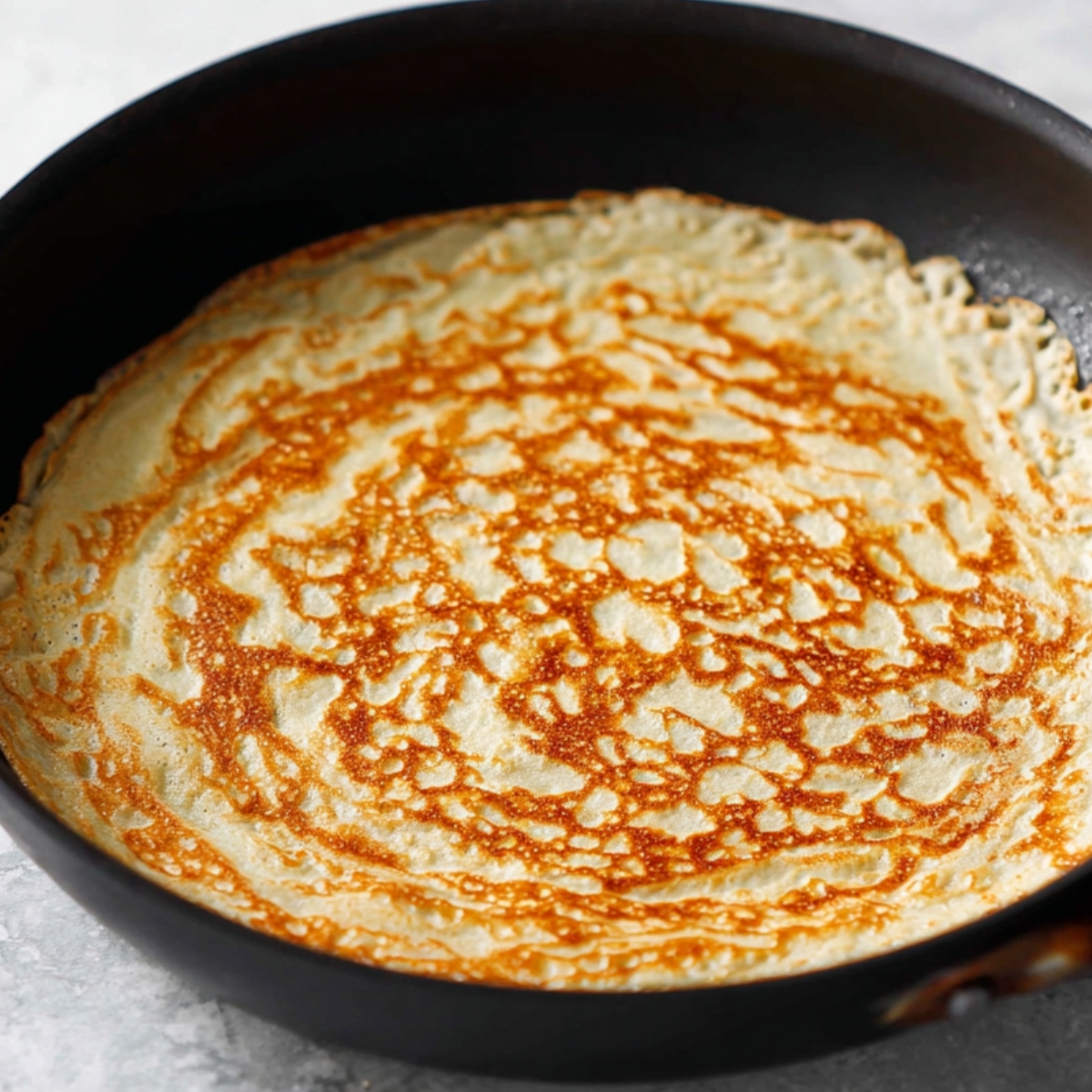 A golden-brown crepe cooking in a pan.