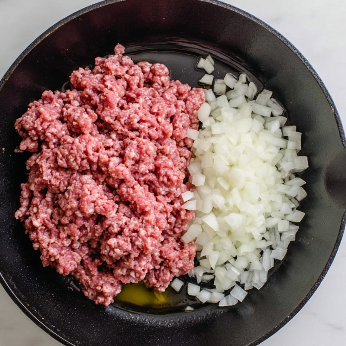 Raw ground beef and diced onions in a skillet
