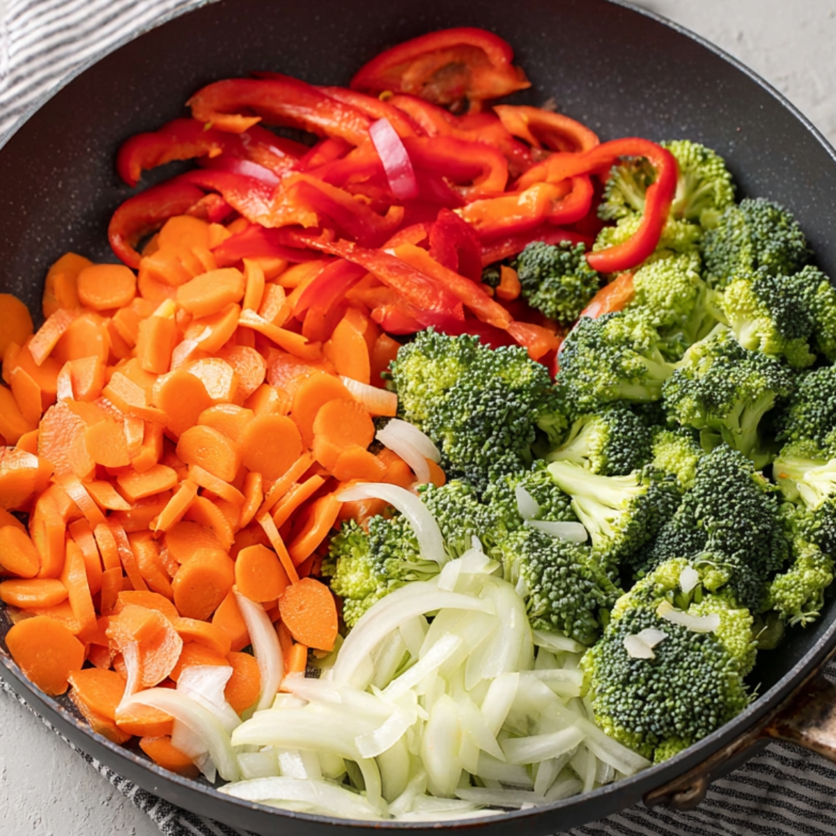 Chopped broccoli, red bell peppers, carrots, onions, and green onions arranged in a skillet, ready to be cooked.