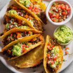 Crispy Ground Beef Tacos topped with guacamole and pico de gallo