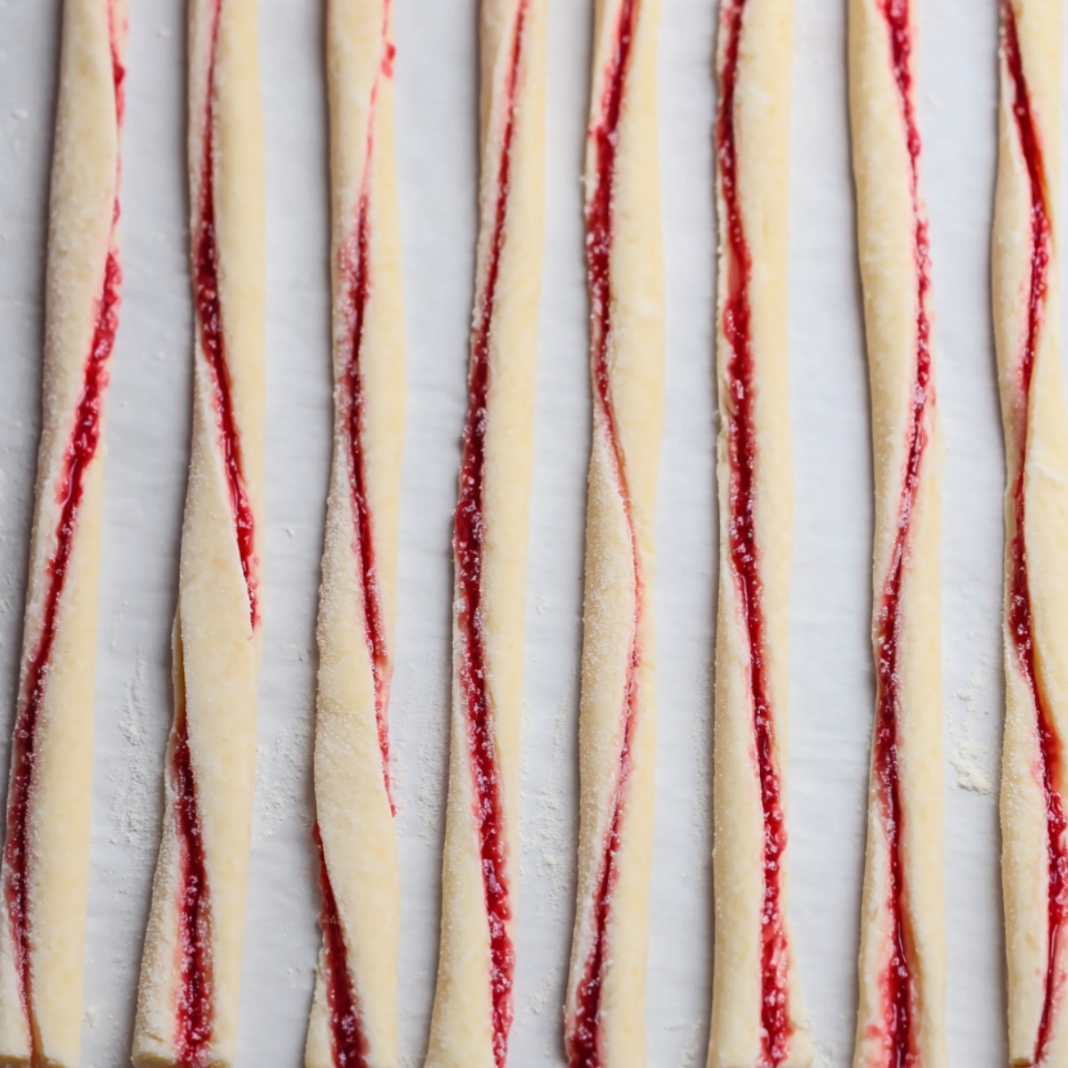 The image shows strips of dough filled with raspberry jam, ready to be twisted.