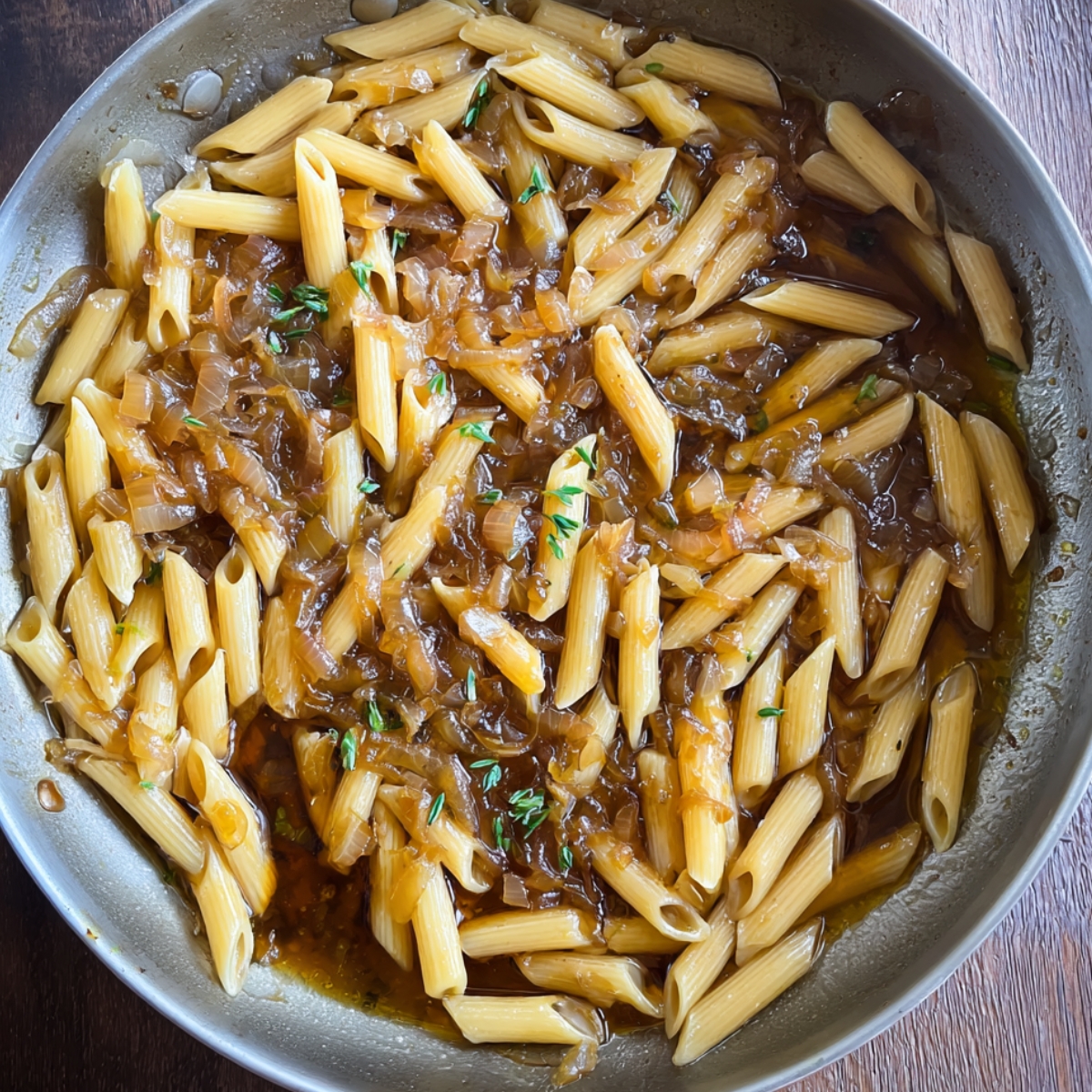 Penne pasta cooked in a savory onion sauce, garnished with thyme.