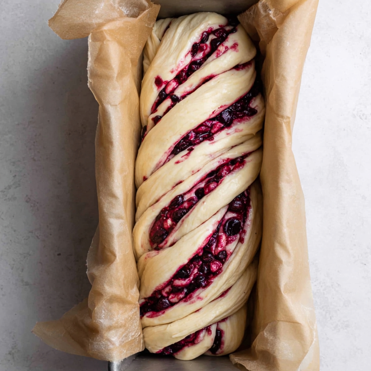 Berry-filled dough twisted and ready for baking in a loaf pan, lined with parchment paper.