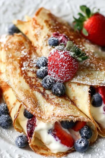 Two delicious Homemade Crepes filled with berries and cream, topped with powdered sugar.