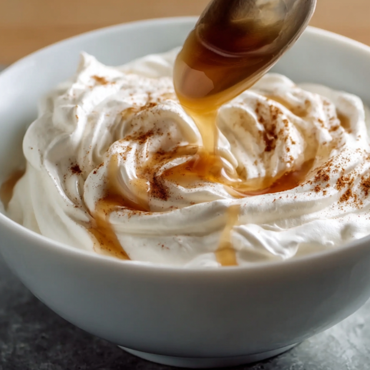 Whipped cream topped with cinnamon and syrup being drizzled into a bowl.