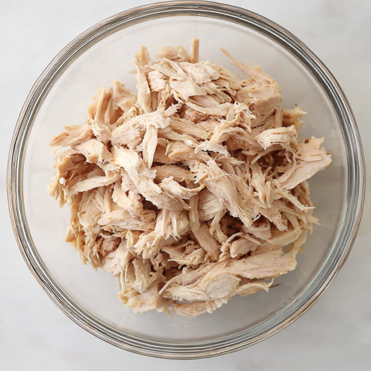 Shredded cooked chicken in a glass bowl