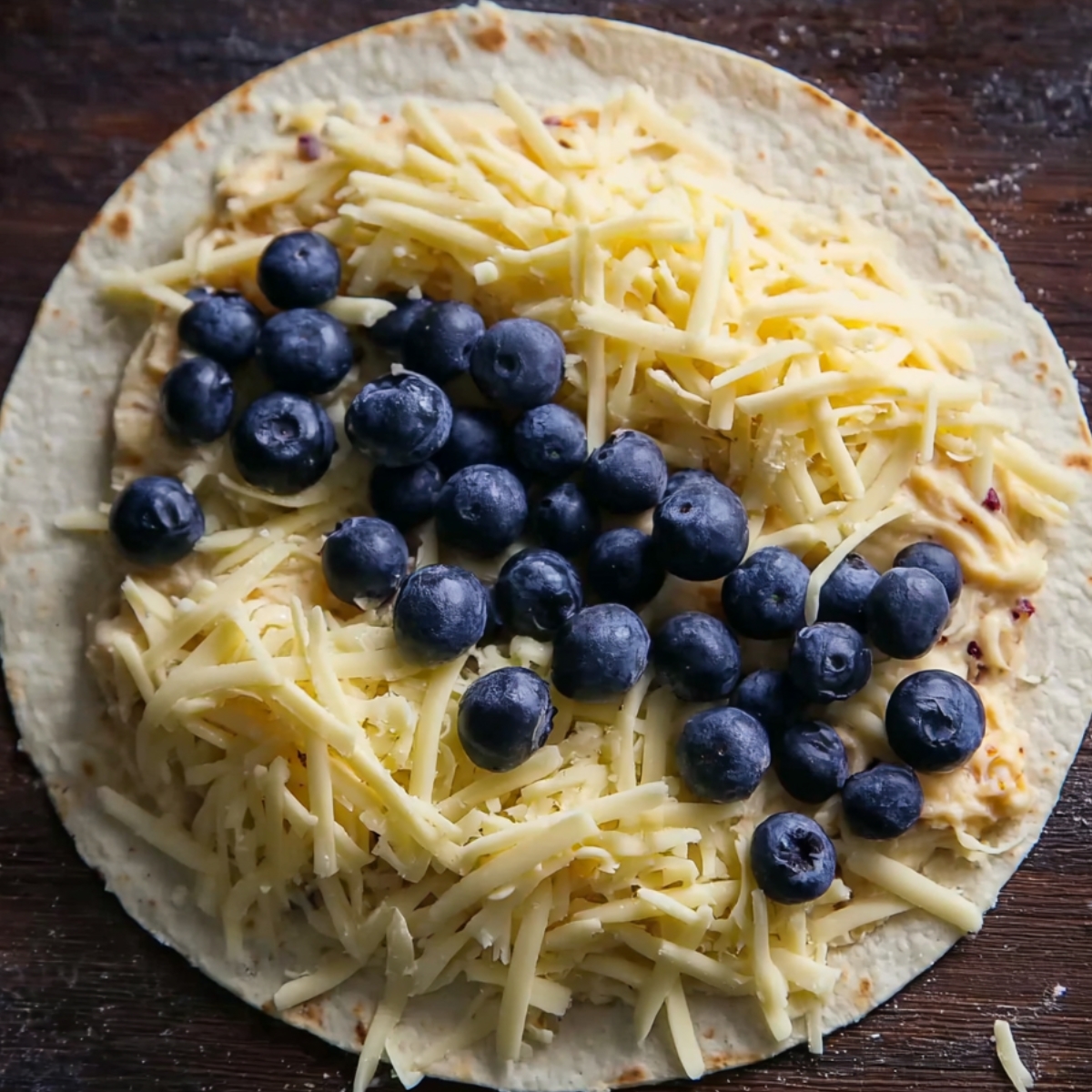 A tortilla filled with shredded cheese and fresh blueberries, ready to be folded into a blueberry breakfast quesadilla.