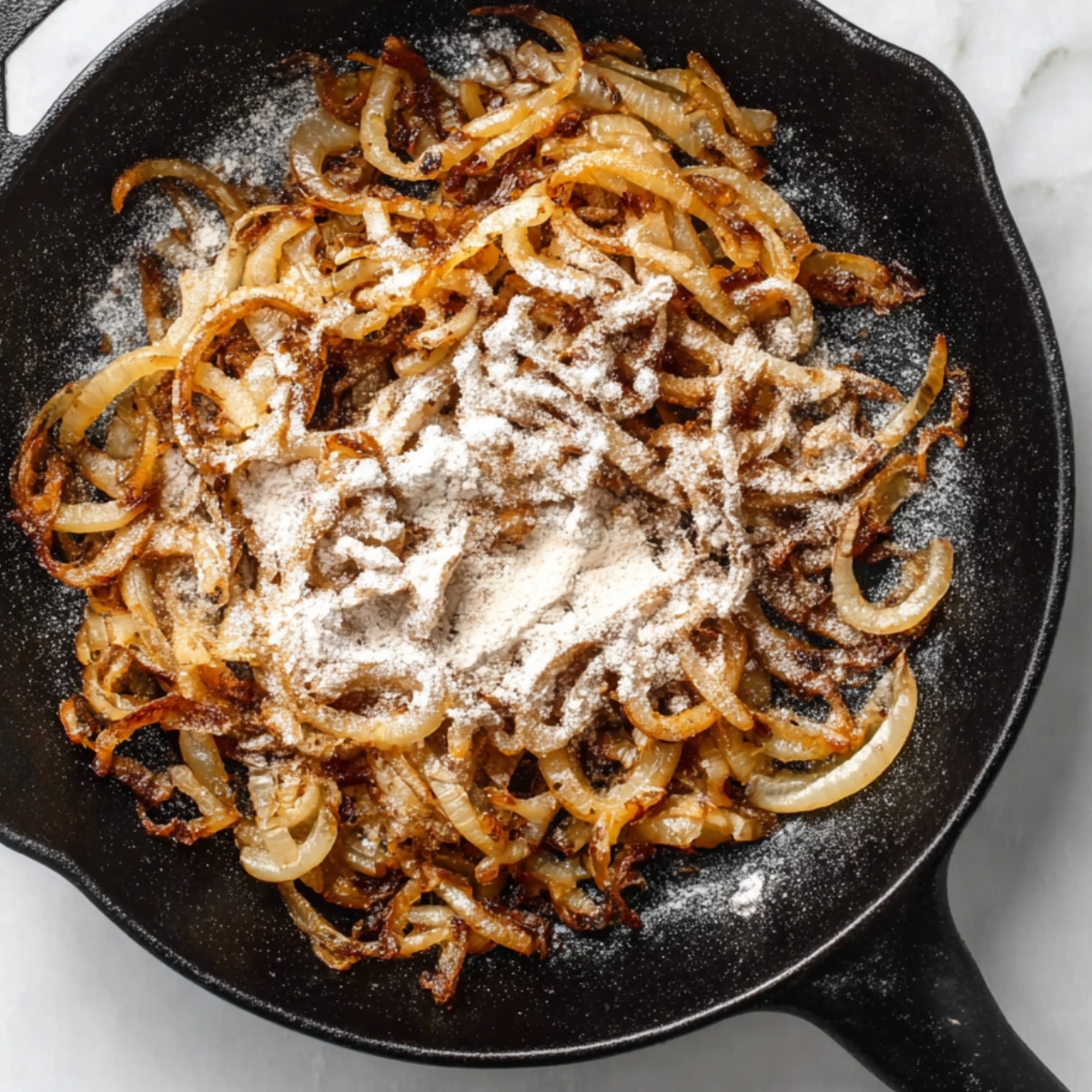 Caramelized onions sprinkled with flour in a skillet.