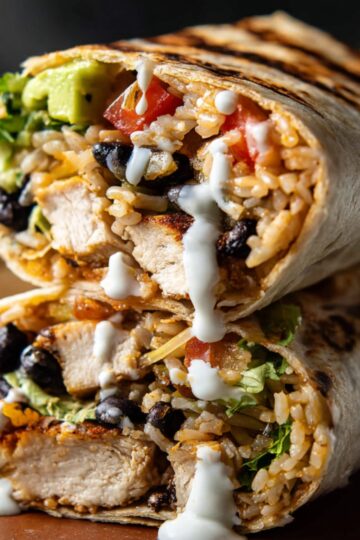 A chipotle ranch grilled chicken burritos filled with rice, black beans, tomatoes, lettuce, avocado, and a drizzle of ranch sauce.