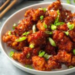 crispy chilli chicken pieces coated in a sweet chili sauce, garnished with green onions.