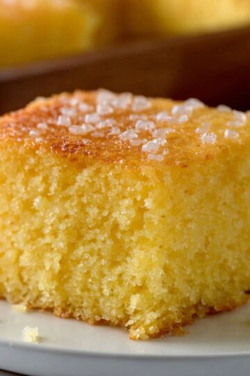 A close-up of a slice of lemon cake topped with a sprinkle of coarse sugar, served on a plate.