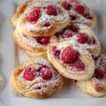 Raspberry danishes with creamy filling and fresh raspberries, dusted with powdered sugar, served on a white plate.