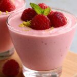 The image shows raspberry mousse served in a glass, topped with fresh raspberries and mint. Would you like a recipe or further instructions on making this mousse?