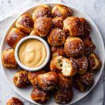 Golden soft pretzel bites with coarse salt and creamy dipping sauce on a plate.