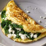 An spinach and feta omelet with spinach and crumbled feta cheese, cooked and folded in a non-stick pan.
